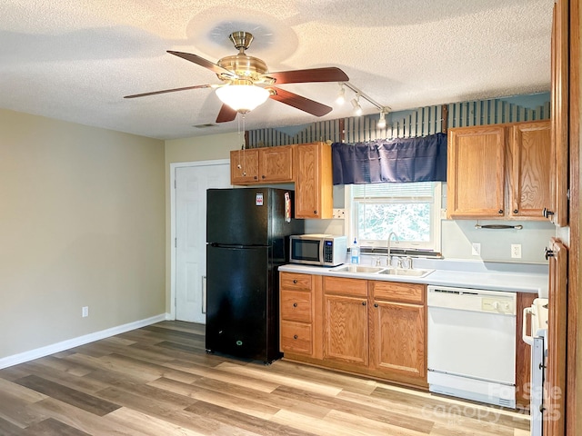 kitchen featuring freestanding refrigerator, dishwasher, a sink, stainless steel microwave, and light wood finished floors