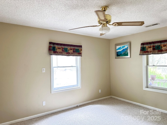 carpeted empty room featuring a wealth of natural light, visible vents, a textured ceiling, and ceiling fan