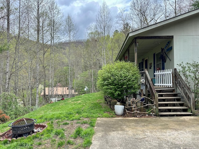 view of yard featuring an outdoor fire pit, a view of trees, and covered porch