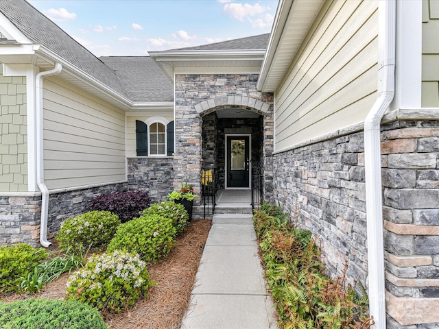doorway to property with roof with shingles and stone siding
