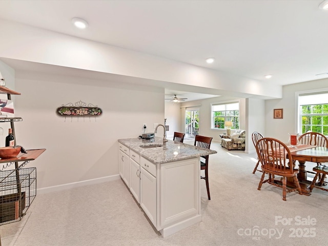 kitchen with a peninsula, a ceiling fan, a sink, and light colored carpet