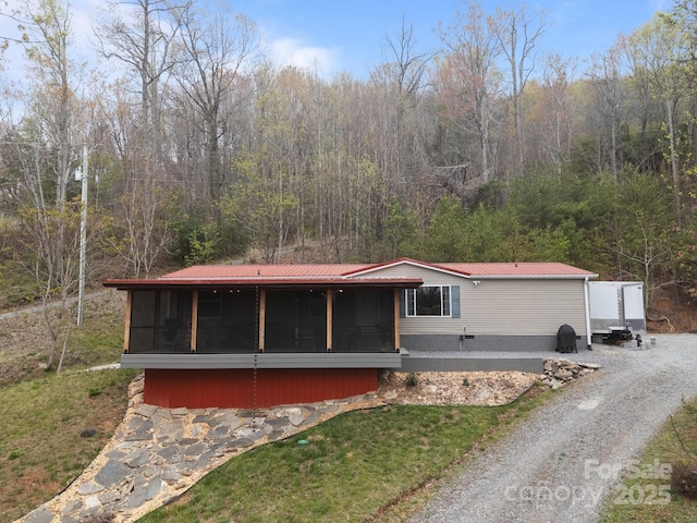 view of front facade with a wooded view, metal roof, and a sunroom