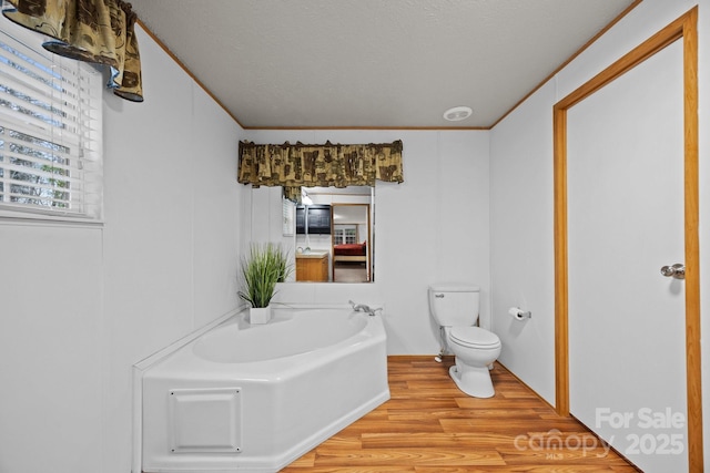 full bath featuring toilet, a bath, wood finished floors, and crown molding