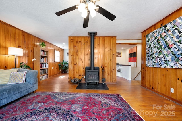 living room featuring wood walls, a ceiling fan, a wood stove, and wood finished floors