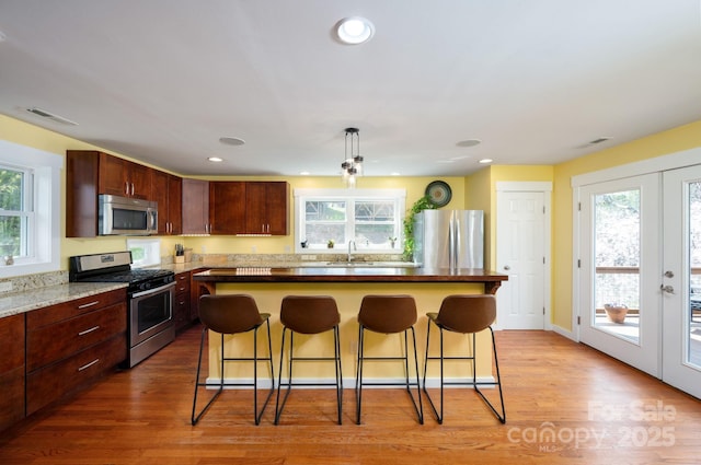 kitchen featuring stainless steel appliances, visible vents, light wood-style floors, a kitchen island, and a breakfast bar area