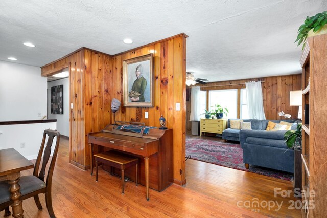 dining space with a textured ceiling, recessed lighting, wood walls, wood finished floors, and ceiling fan