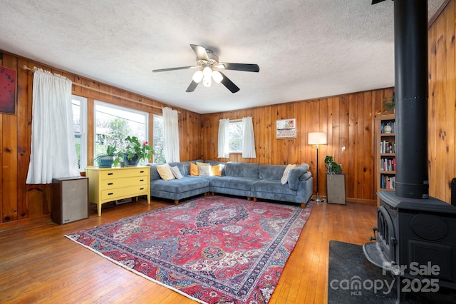 living area featuring ceiling fan, a textured ceiling, a wood stove, and wood-type flooring