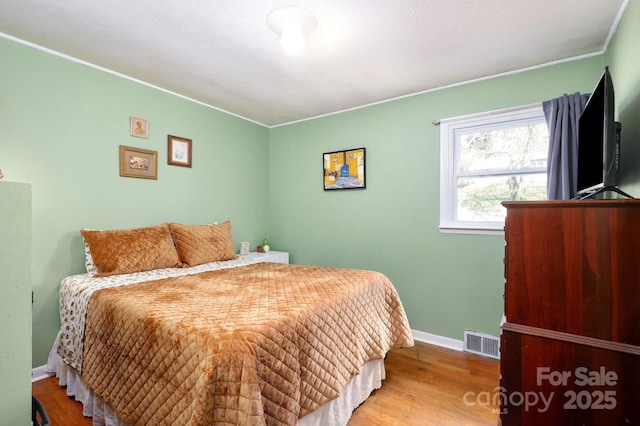 bedroom with wood finished floors, visible vents, baseboards, and ornamental molding