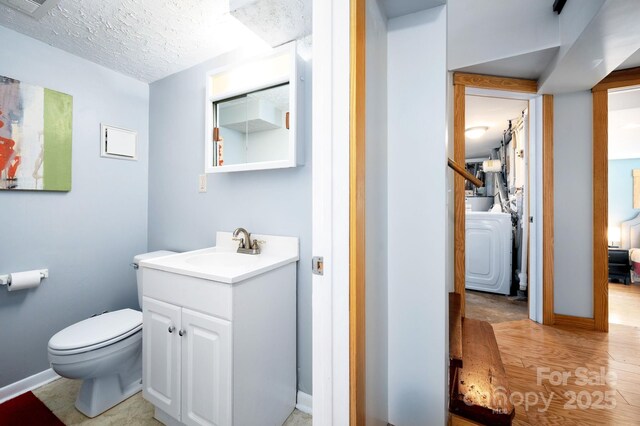 bathroom featuring wood finished floors, vanity, washer / dryer, baseboards, and toilet
