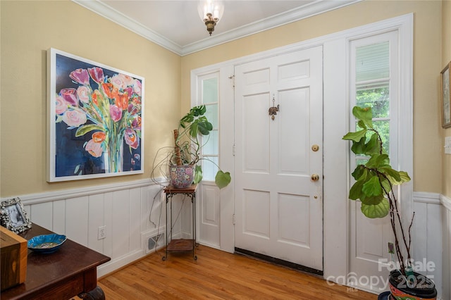 foyer entrance with visible vents, a wainscoted wall, light wood finished floors, ornamental molding, and a decorative wall