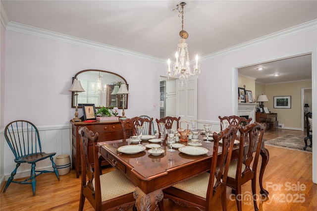 dining space featuring an inviting chandelier, crown molding, light wood-style flooring, and wainscoting