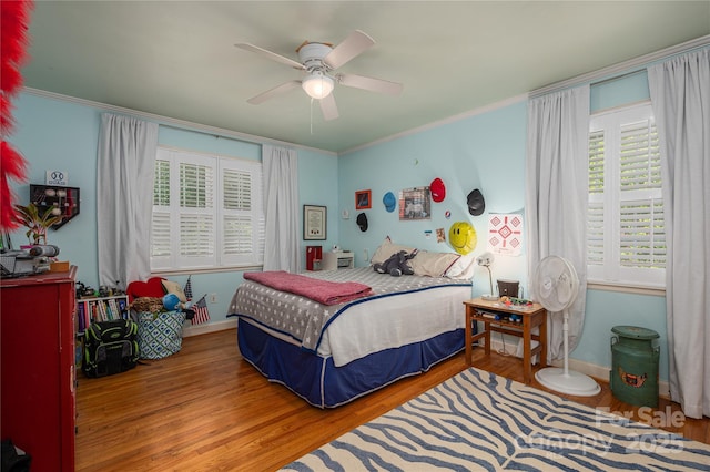 bedroom featuring wood finished floors, crown molding, a ceiling fan, and multiple windows