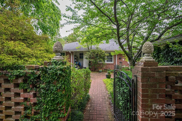 view of property hidden behind natural elements with a shingled roof, a gate, and brick siding