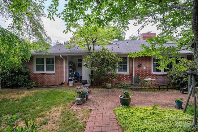back of property featuring a lawn, a patio, a chimney, and brick siding