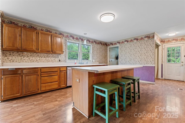 kitchen with brown cabinets, wallpapered walls, stainless steel dishwasher, and light wood-type flooring