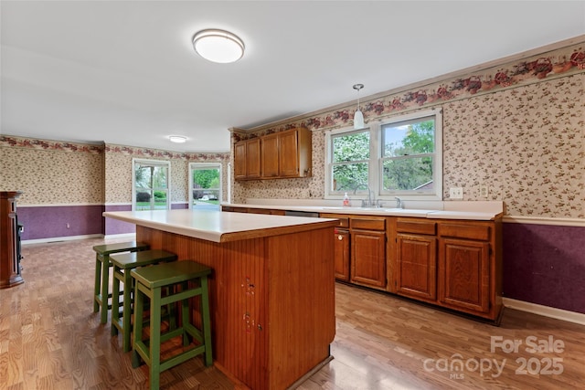 kitchen featuring wallpapered walls, light wood-style flooring, light countertops, a wainscoted wall, and brown cabinetry