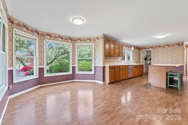 kitchen featuring wallpapered walls, light countertops, brown cabinets, stainless steel dishwasher, and light wood finished floors