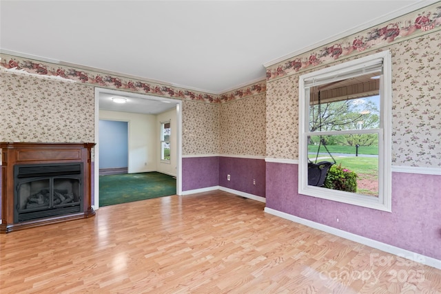 unfurnished living room featuring a wainscoted wall, plenty of natural light, wood finished floors, and wallpapered walls
