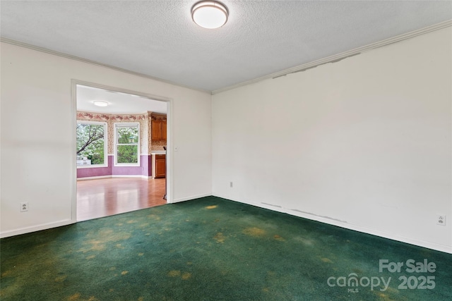 spare room featuring dark carpet, a textured ceiling, baseboards, and ornamental molding