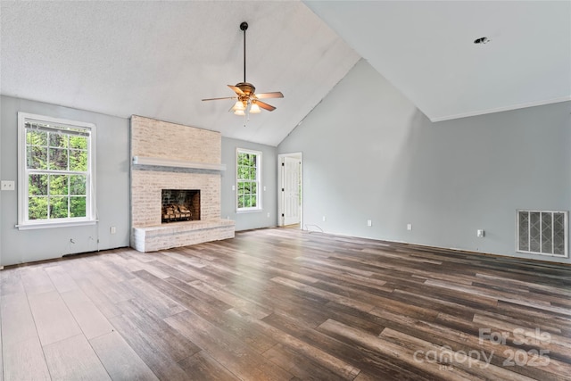 unfurnished living room with visible vents, a brick fireplace, ceiling fan, wood finished floors, and high vaulted ceiling