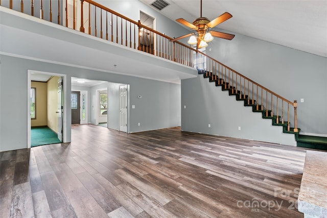 unfurnished living room with ornamental molding, a high ceiling, a ceiling fan, visible vents, and wood finished floors