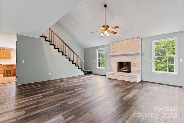 unfurnished living room featuring dark wood-style flooring, ceiling fan, stairway, and a brick fireplace