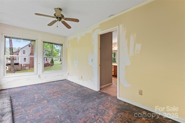 spare room with baseboards, ornamental molding, a ceiling fan, a textured ceiling, and carpet floors