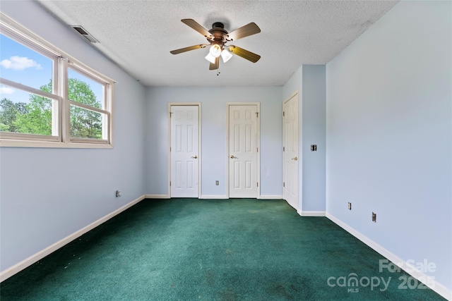 unfurnished bedroom featuring visible vents, baseboards, dark carpet, a textured ceiling, and multiple closets