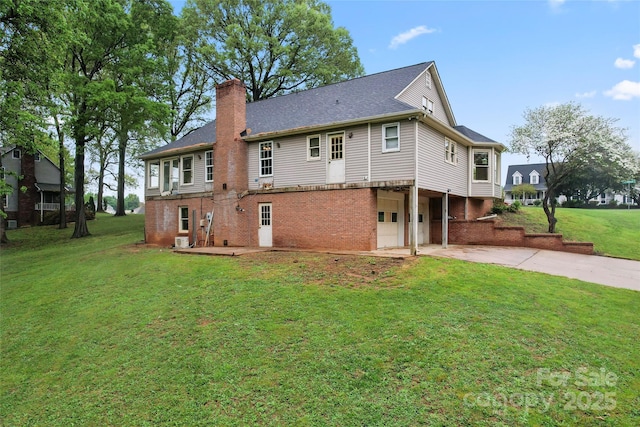 rear view of house featuring a garage, a yard, brick siding, a chimney, and concrete driveway