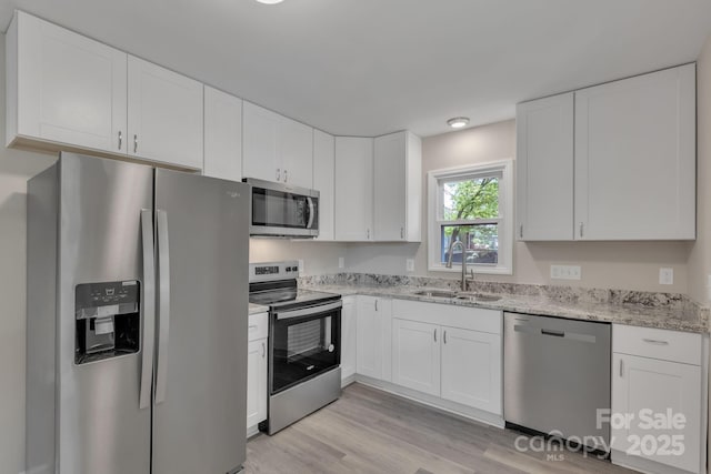 kitchen with stainless steel appliances, a sink, white cabinets, light wood-style flooring, and light stone counters