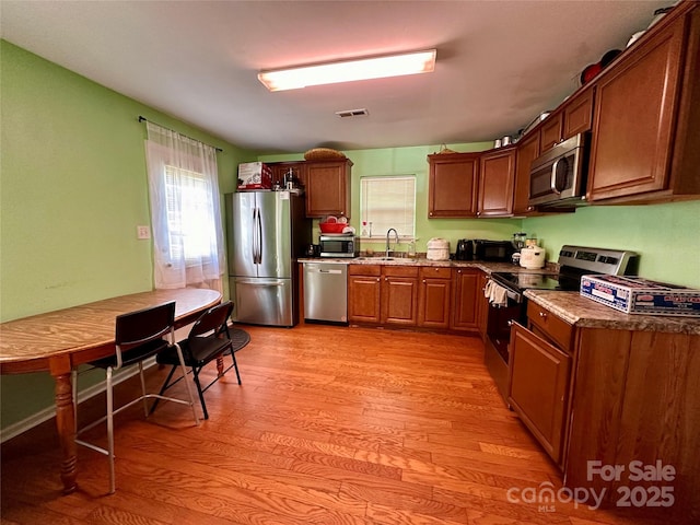 kitchen featuring light wood-type flooring, visible vents, brown cabinets, appliances with stainless steel finishes, and a sink