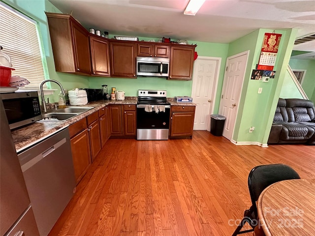 kitchen featuring stainless steel appliances, open floor plan, light wood-type flooring, and a sink