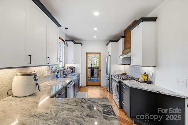 kitchen featuring white cabinets, wall chimney exhaust hood, light stone counters, and stainless steel appliances