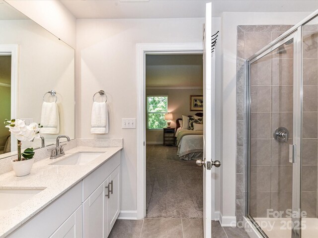 ensuite bathroom with a shower stall, tile patterned floors, baseboards, and double vanity
