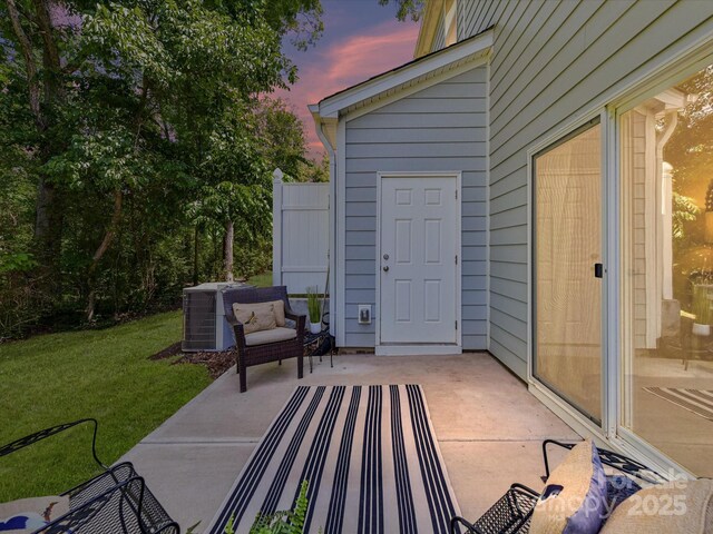 patio terrace at dusk featuring cooling unit and a lawn