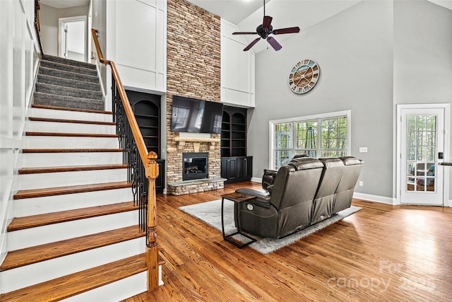 living area with a ceiling fan, a stone fireplace, wood finished floors, high vaulted ceiling, and baseboards