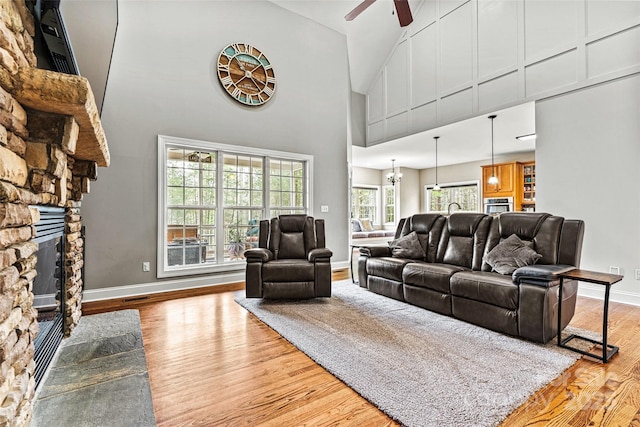 living area with a ceiling fan, a fireplace, wood finished floors, baseboards, and high vaulted ceiling
