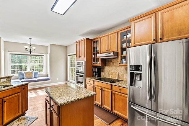 kitchen with under cabinet range hood, light stone counters, light wood finished floors, a chandelier, and stainless steel appliances