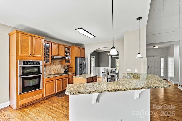 kitchen with brown cabinets, a breakfast bar area, arched walkways, stainless steel appliances, and a peninsula