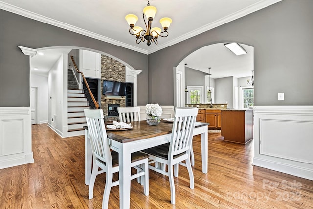 dining space featuring ornamental molding, a wainscoted wall, a chandelier, arched walkways, and light wood-style flooring