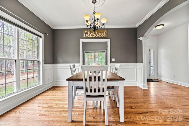 dining area with arched walkways, a chandelier, a wealth of natural light, and light wood-style floors