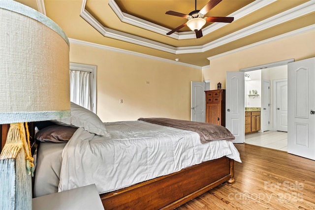 bedroom with ceiling fan, crown molding, light wood-type flooring, a raised ceiling, and ensuite bathroom