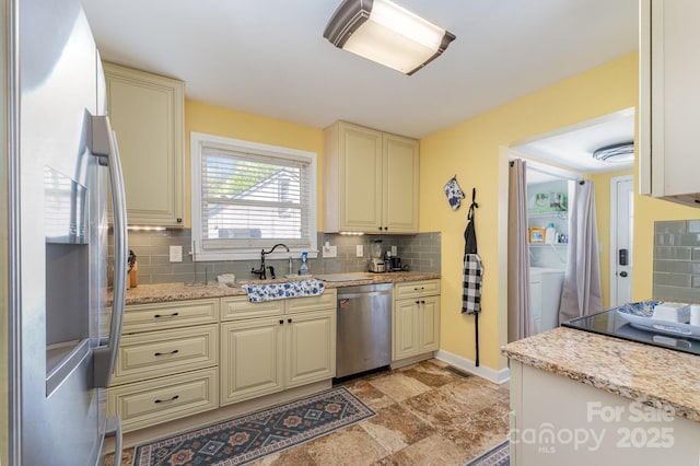 kitchen with tasteful backsplash, cream cabinetry, appliances with stainless steel finishes, light stone counters, and a sink