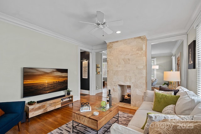 living room with a tile fireplace, a ceiling fan, ornamental molding, wood-type flooring, and baseboards