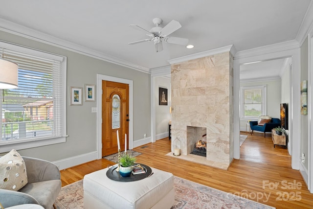 living area with a ceiling fan, crown molding, light wood-style floors, a tiled fireplace, and baseboards