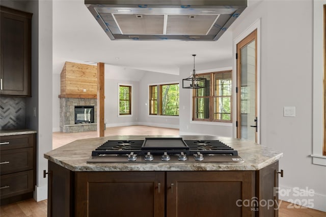 29 Wild Deer Trl, Zirconia, NC 28790 - kitchen featuring ventilation hood, stainless steel gas cooktop, dark brown cabinetry, a stone fireplace, and vaulted ceiling