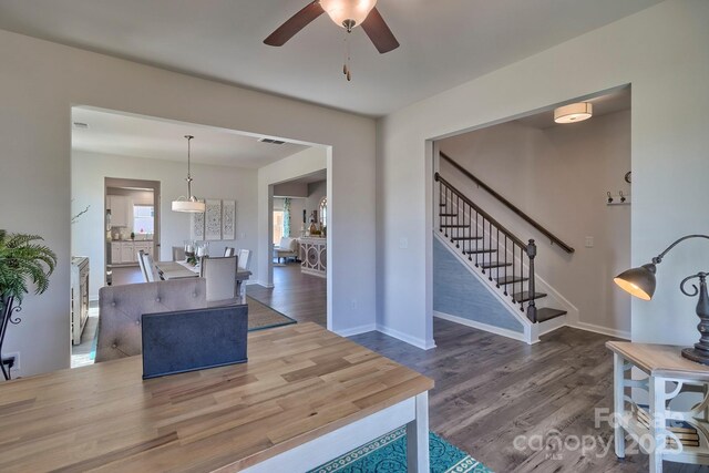living area with visible vents, baseboards, wood finished floors, stairway, and a ceiling fan