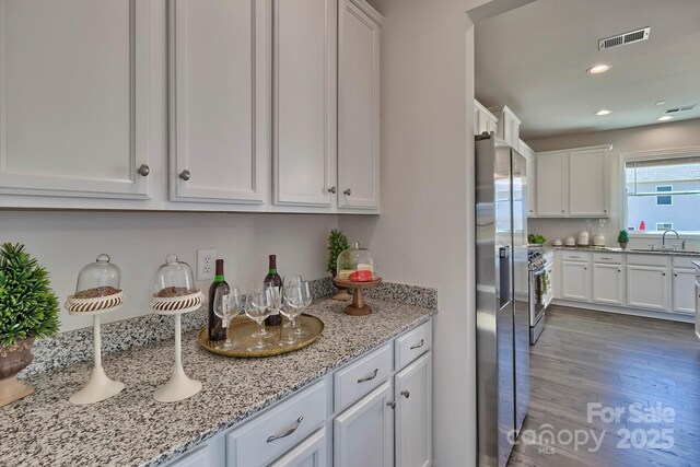 kitchen with stainless steel fridge, light stone counters, visible vents, white cabinets, and wood finished floors