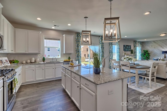 kitchen featuring a center island, gas stove, a sink, dark wood-style floors, and light stone counters
