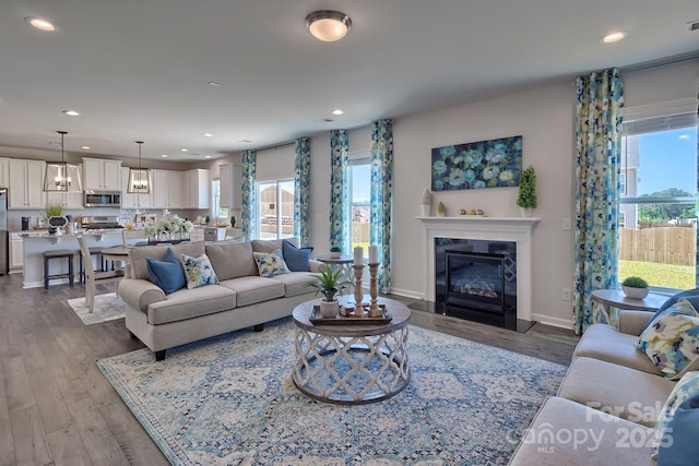 living area featuring recessed lighting, a glass covered fireplace, baseboards, and wood finished floors